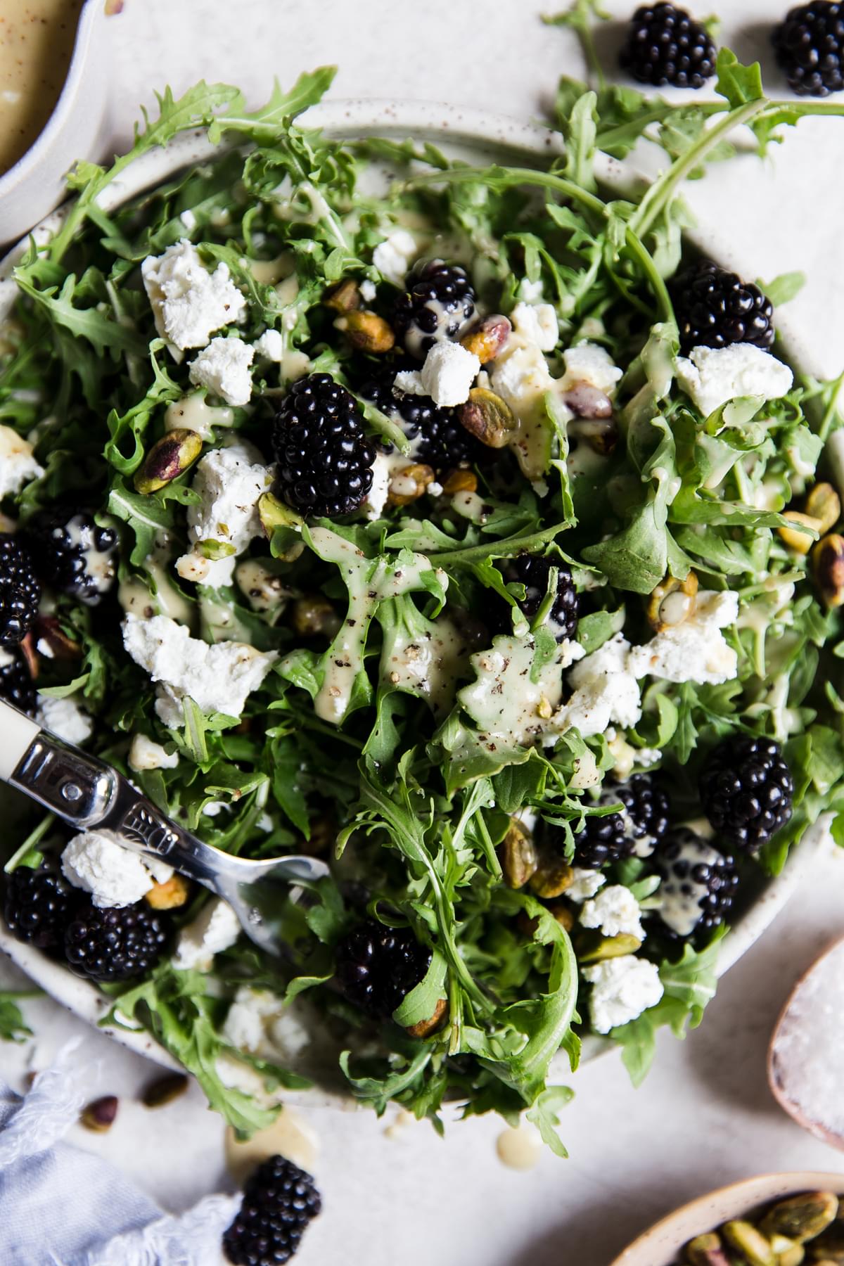 Arugula salad topped with blackberries, goat cheese, pistachios and honey mustard salad dressing on a plate