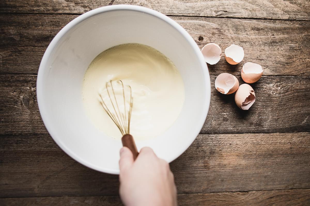 a bowl of eggs and cream being whisked with wire whisk