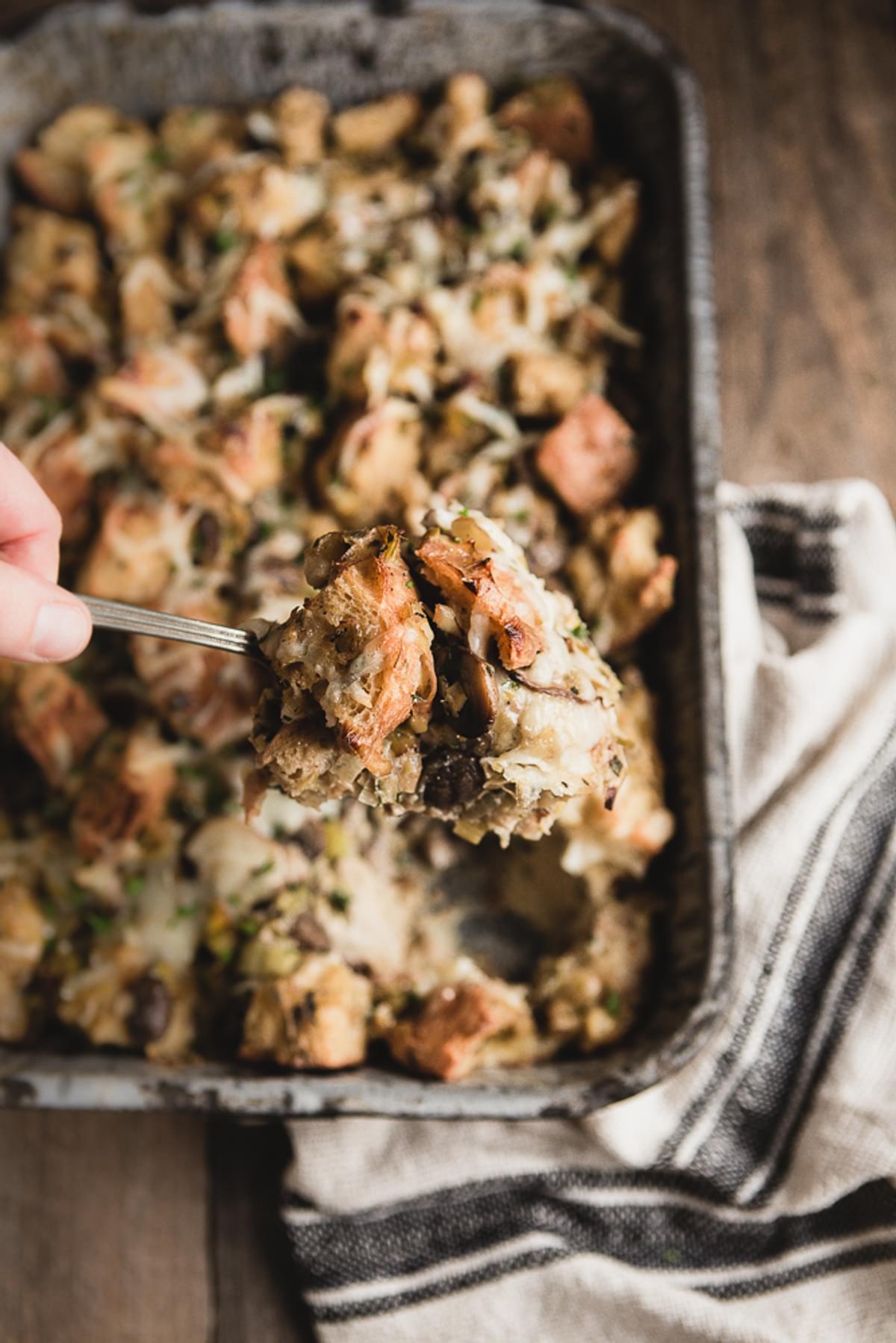 large spoon scooping mushroom and leek bread pudding out of a baking dish