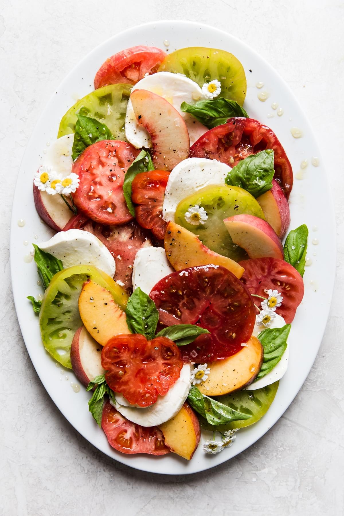 Peach and tomato caprese salad with heirloom tomatoes and fresh mozzarella on white plate with fresh basil.