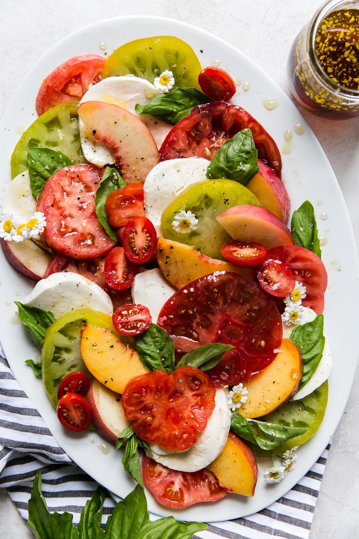 Peach, tomato and mozzarella caprese salad topped with fresh basil and a jar of homemade salad dressing.