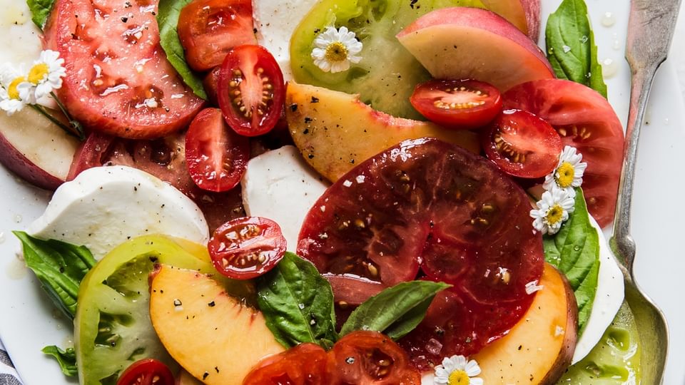 peach and tomato caprese salad with fresh mozzarella, basil and olive oil on a large white platter.