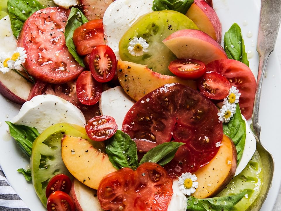 peach and tomato caprese salad with fresh mozzarella, basil and olive oil on a large white platter.