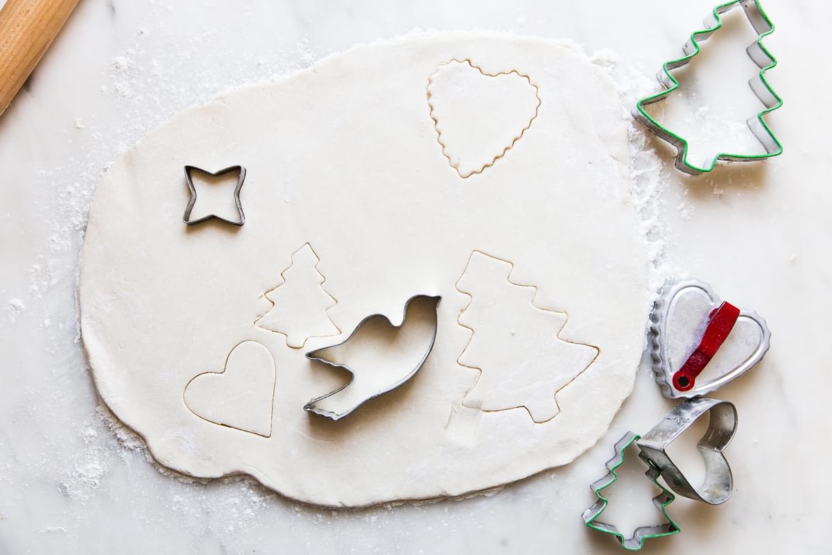 Sour Cream Sugar Cookie dough rolled out with Christmas cookie cutters.