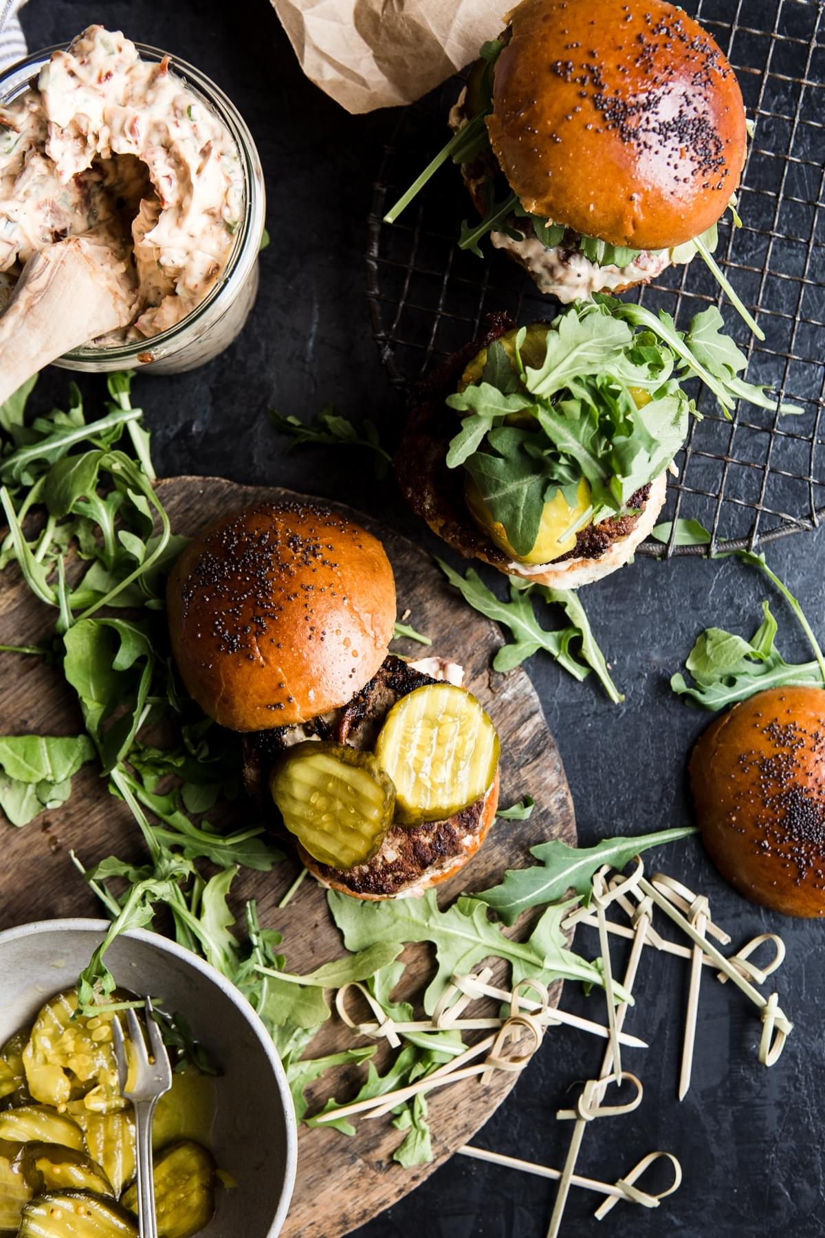 Beef sliders with sun-dried tomato mayo, arugula and sweet and spicy pickles being assembled.