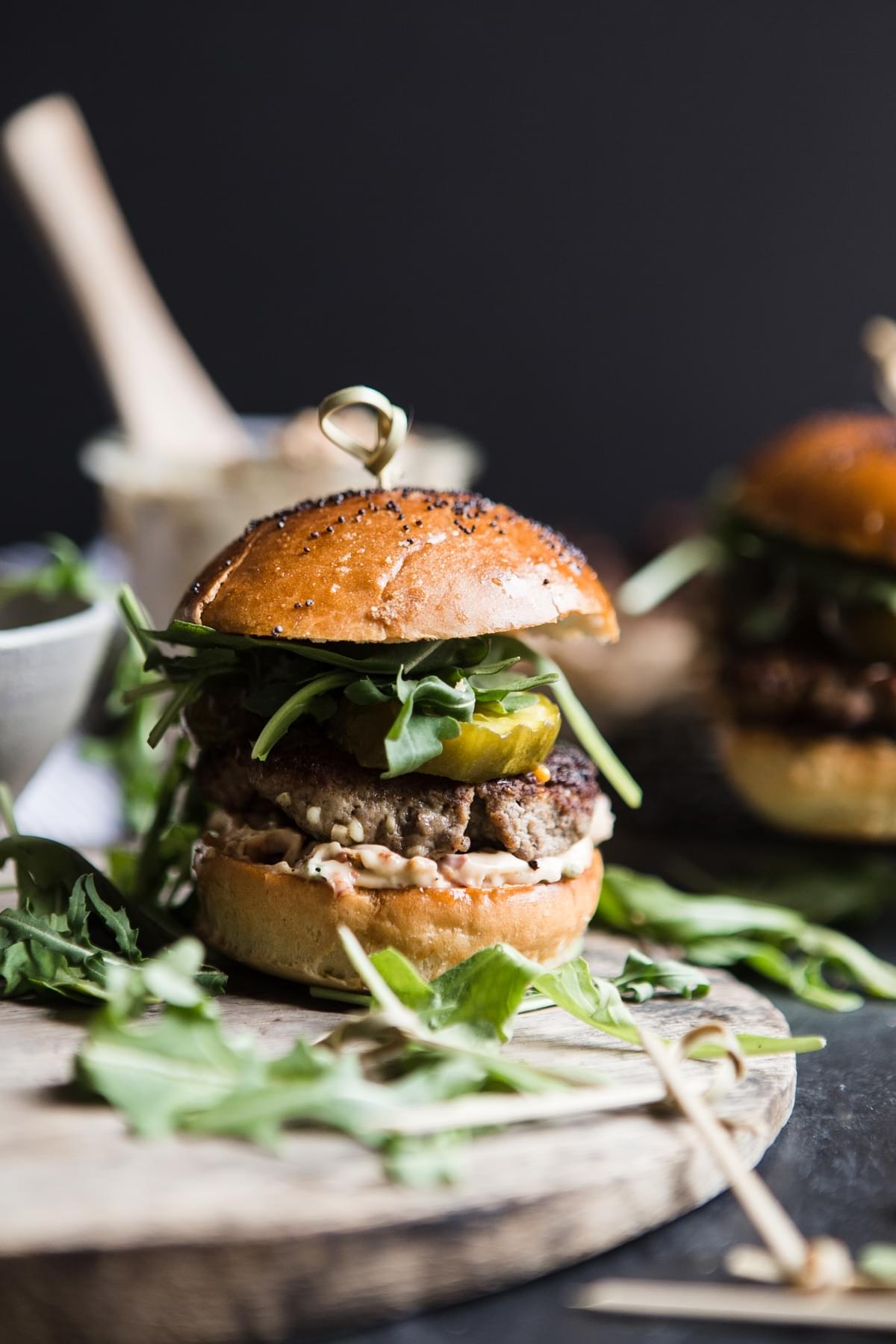 Side view of beef sliders with sun-dried tomato mayo, arugula and sweet and spicy pickles.