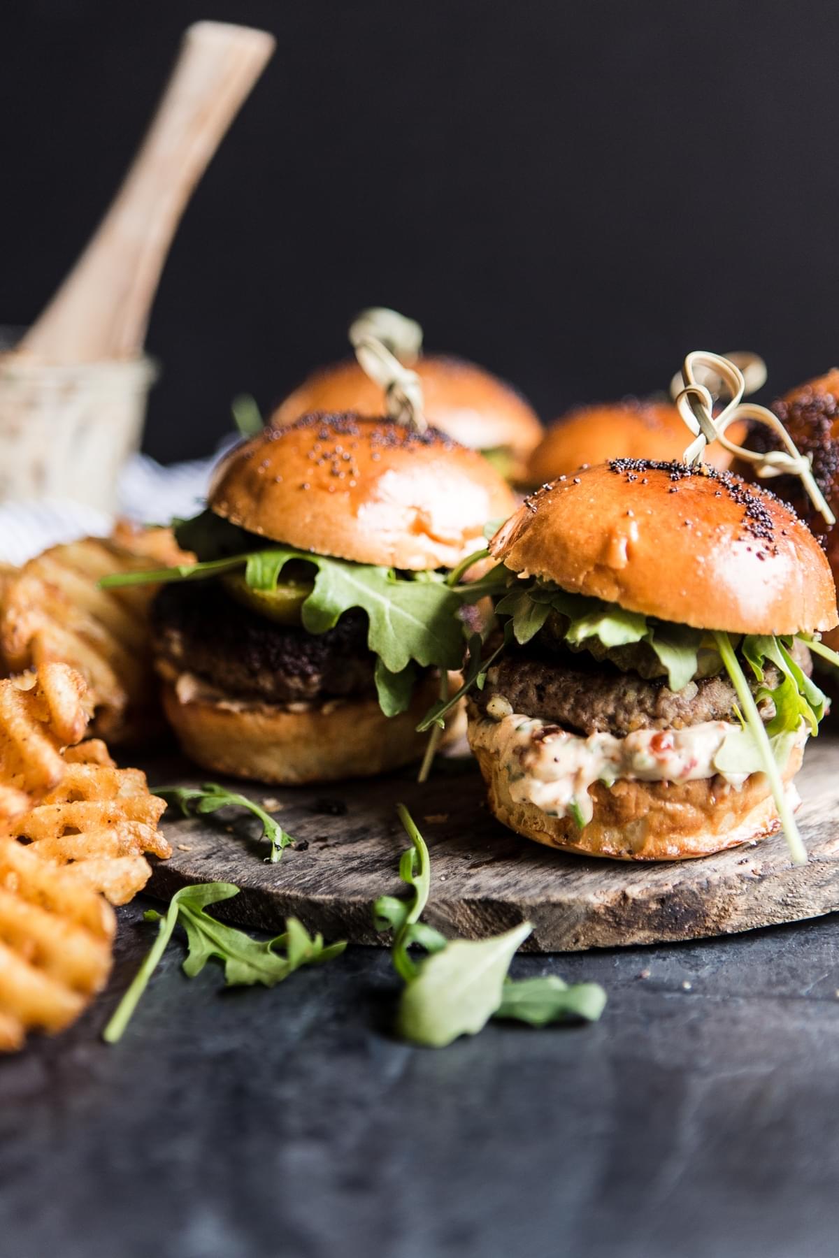 Side view of beef sliders with sun-dried tomato mayo, arugula, sweet and spicy pickles and waffle fries.