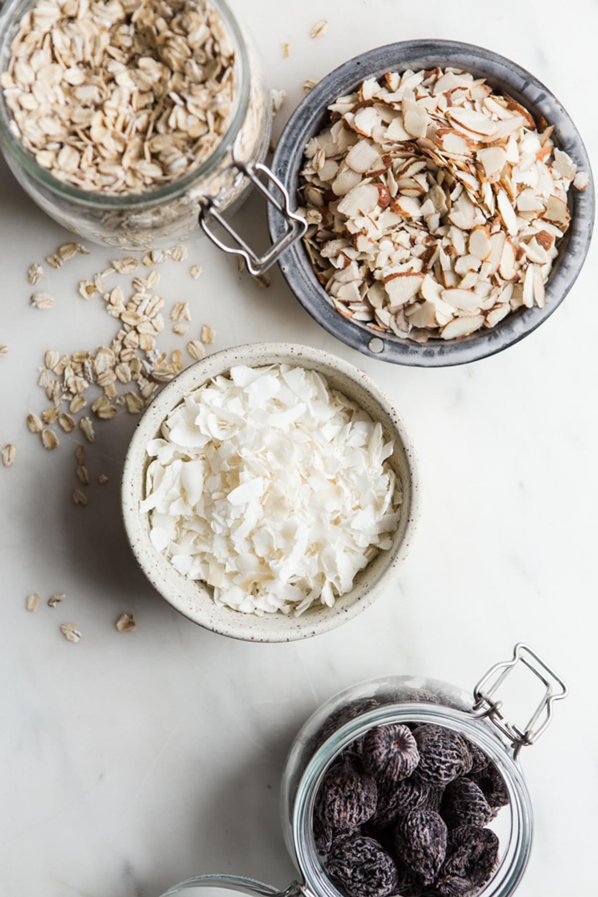 ingredients laid out oats in a jar, sliced almonds, coconut and dried figs in a jar