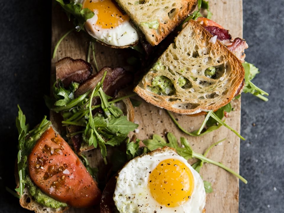 Heirloom BLT with Pesto and Fried Egg cut in half and showing the fried egg on a cutting board