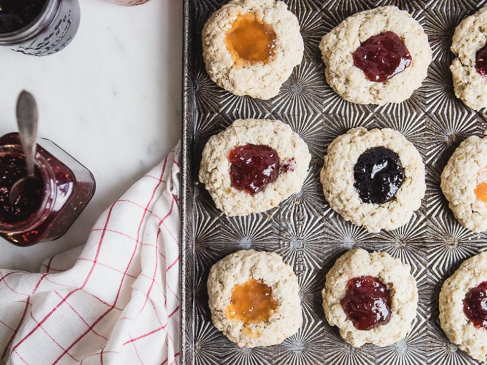 A baking sheet with scones filled with jam a linen and 4 jars of jam, jelly