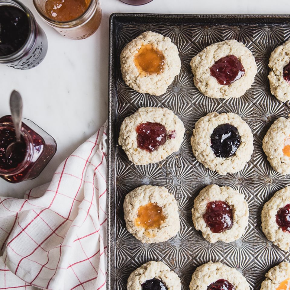 A baking sheet with scones filled with jam a linen and 4 jars of jam, jelly