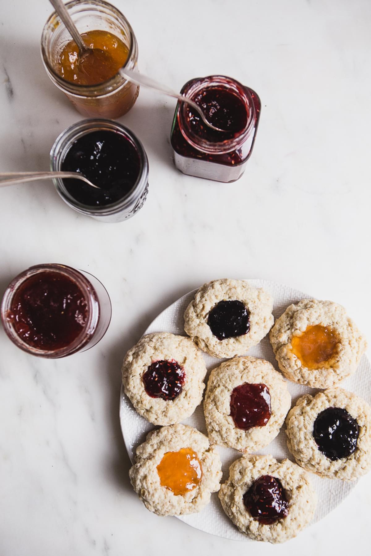 a plate of oat scones with jam on them on a plate and 4 jars of jelly with spoons