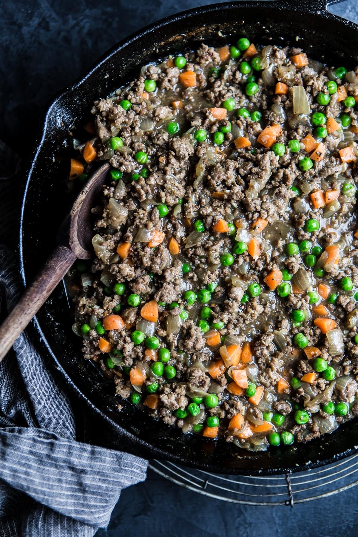 Filling for lamb shepherd's pie, ground lamb, onion, carrots and peas in a cast iron pan with a wooden spoon