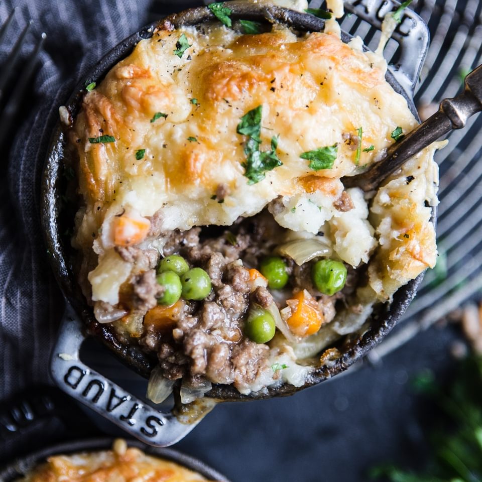 a lamb pie with puff pastry and mashed potatoes sprinkled with gruyere cheese with peas and carrots