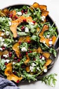 Arugula and roasted acorn squash salad with creamy goat cheese dressing pumpkin seeds and pomegranate seeds on a plate
