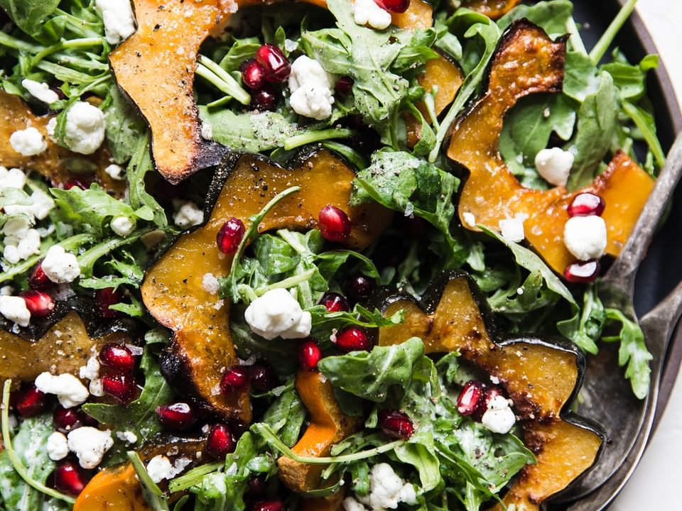 Arugula and roasted acorn squash salad with creamy goat cheese dressing pumpkin seeds and pomegranate seeds on a plate