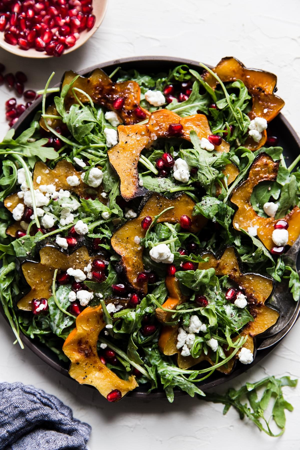 Arugula and roasted acorn squash salad made with a goat cheese dressing pumpkin seeds and pomegranates on a plate.