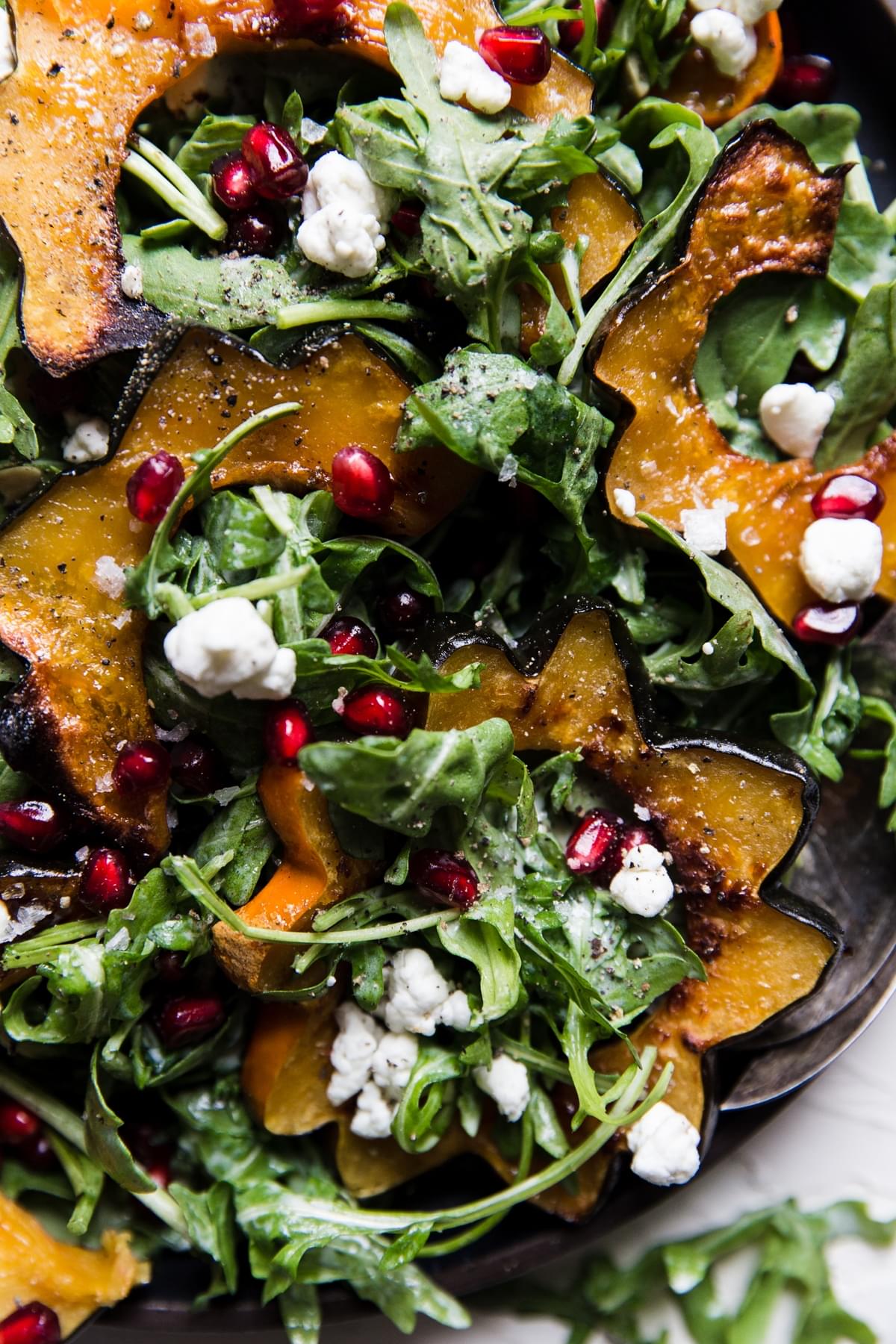 Close up of arugula and roasted acorn squash salad with goat cheese dressing pumpkin seeds and pomegranates on a plate