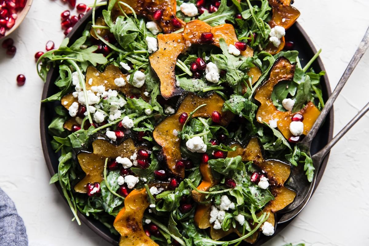 Arugula and roasted squash salad with goat cheese dressing, pumpkin seeds and pomegranates on a plate with serving spoon