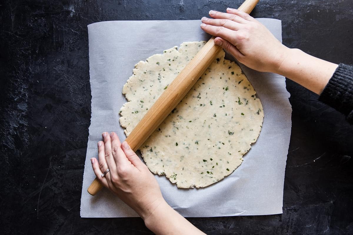 hands rolling out herb galette pastry crust with a rolling pin