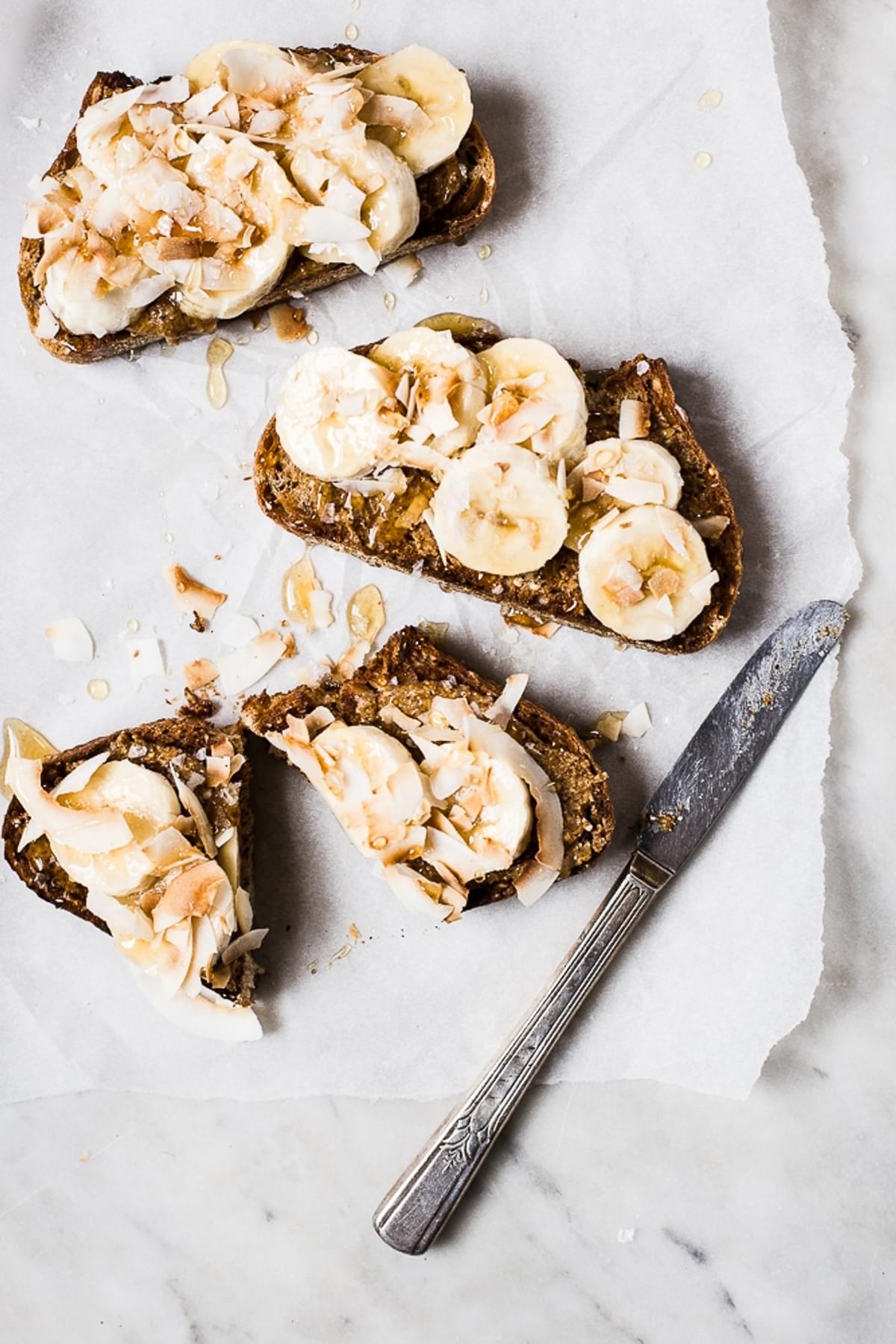 Almond Butter Toast with Bananas, Toasted Coconut, honey and salt on parchment paper