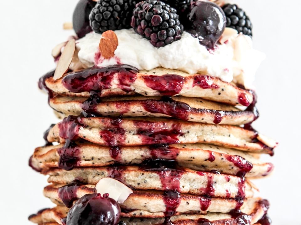 stack of almond poppy seed pancakes topped with whipped cream and fresh berries