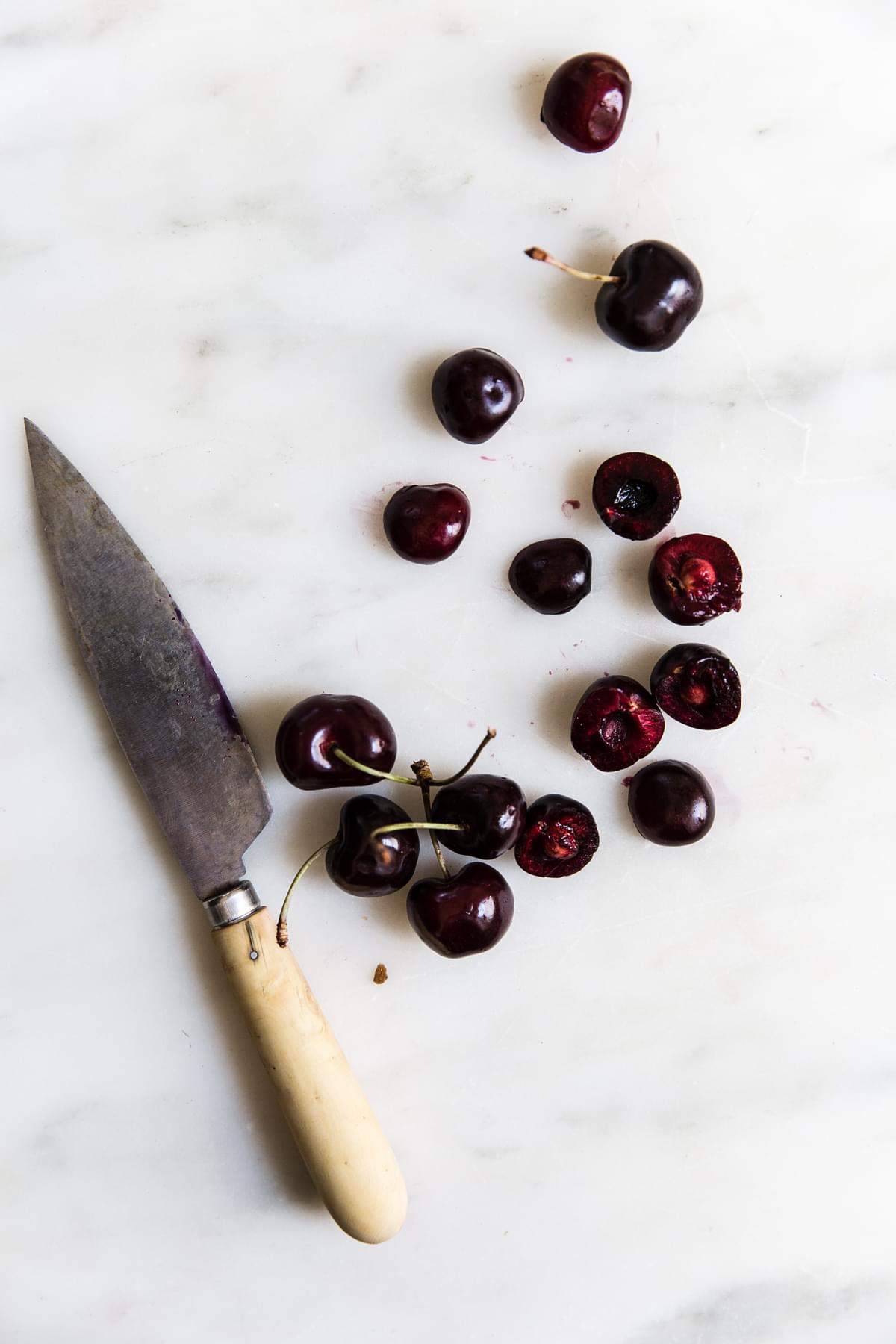 fresh cherries on a marble surface next to a paring knife