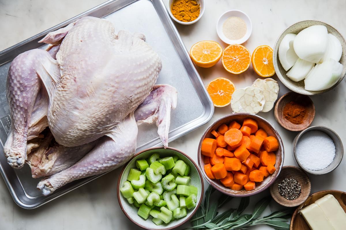 raw thanksgiving turkey on a baking sheet a bowl of carrots, celery, onions, oranges, sage, salt pepper and butter
