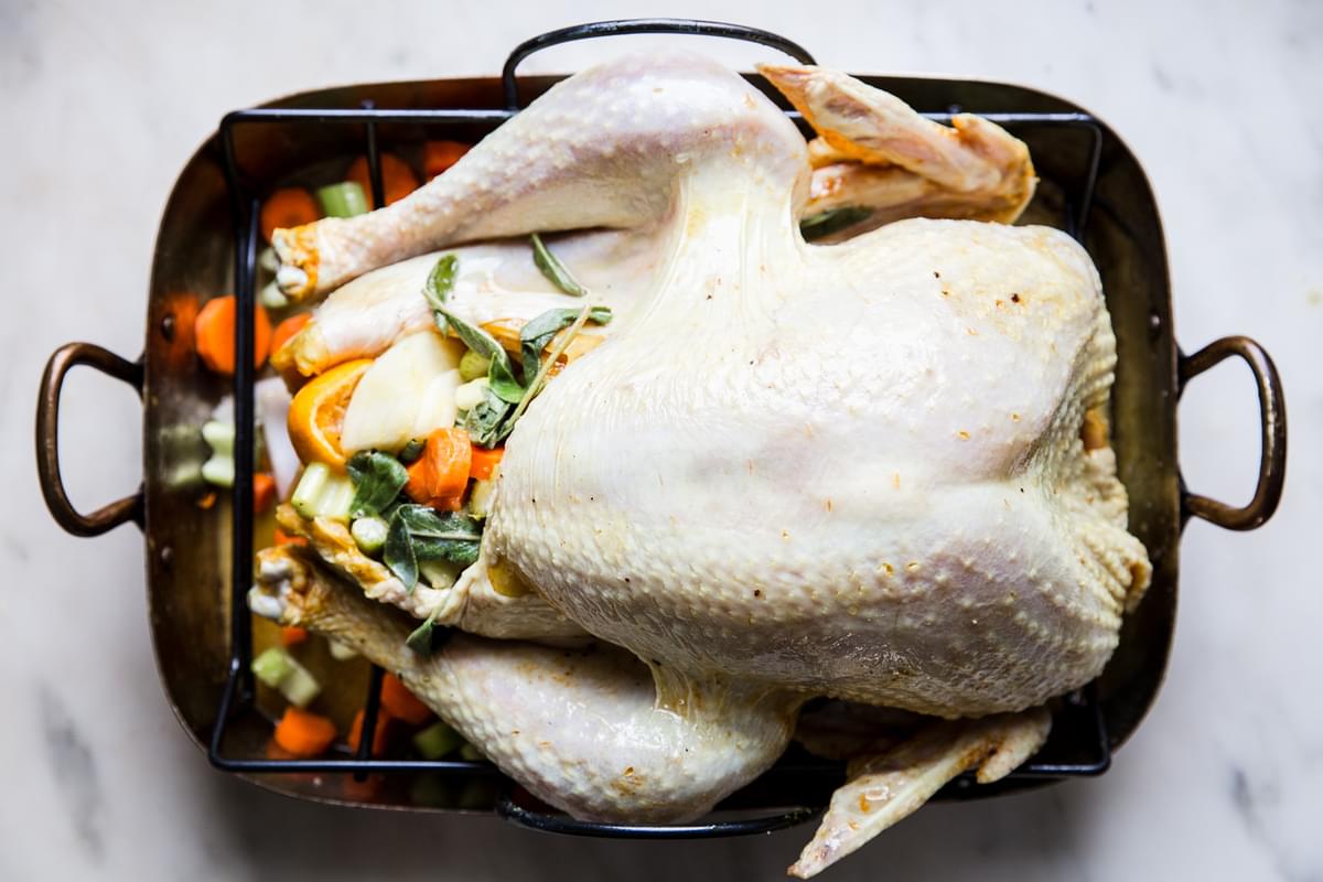 raw dry brined turkey stuffed with herbs and oranges in a roasting pan with vegetables