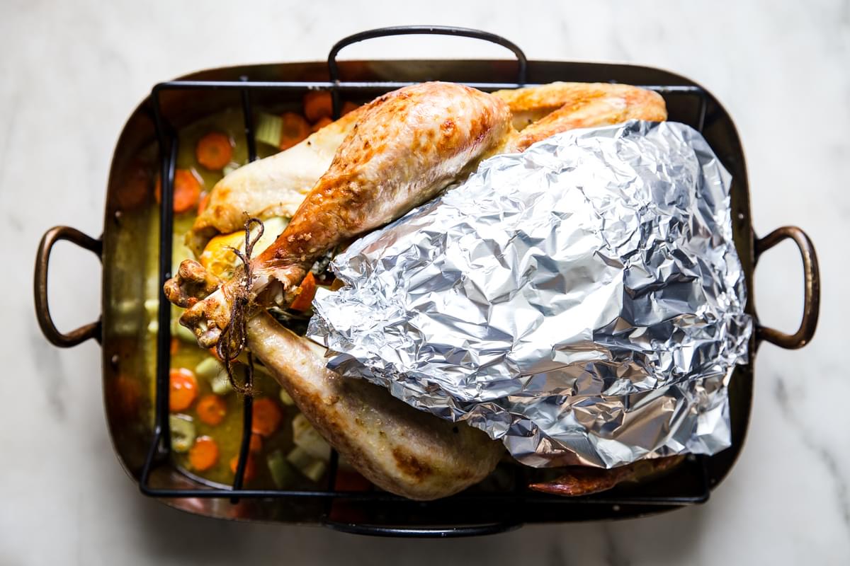 roast turkey recipe with oranges and sage butter halfway cooked in a roasting pan with foil covering the turkey breast