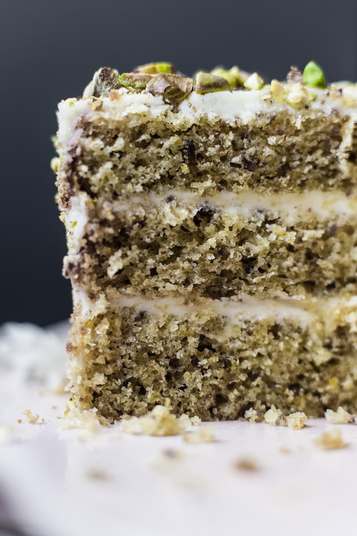 a slice of a 3 layer Yogurt and Olive Oil Pistachio Cake With Lemon Buttercream