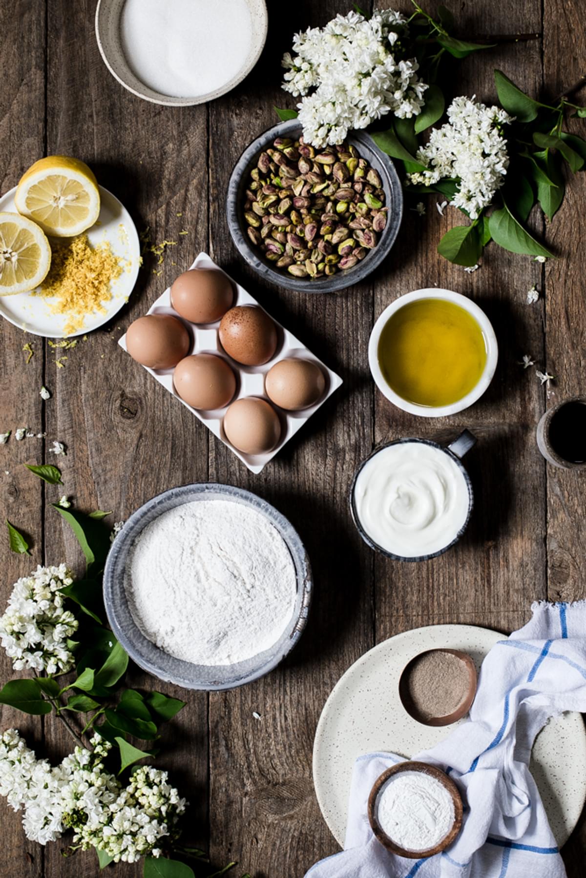 yogurt, flour, eggs, lemons, pistachios, salt, cardamon, olive oil in bowls on the table.