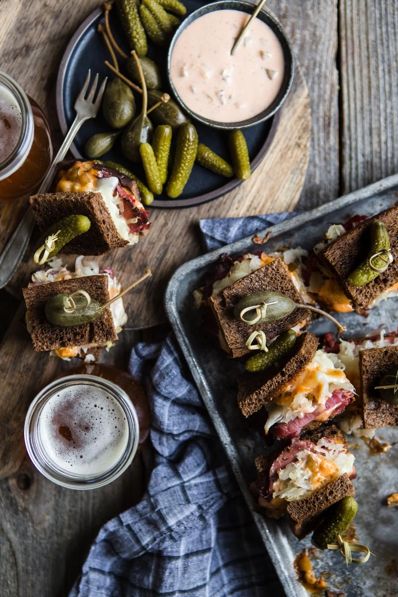 Ruben sandwiches on a platter with homemade Russian dressing served with pickles and a glass of beer