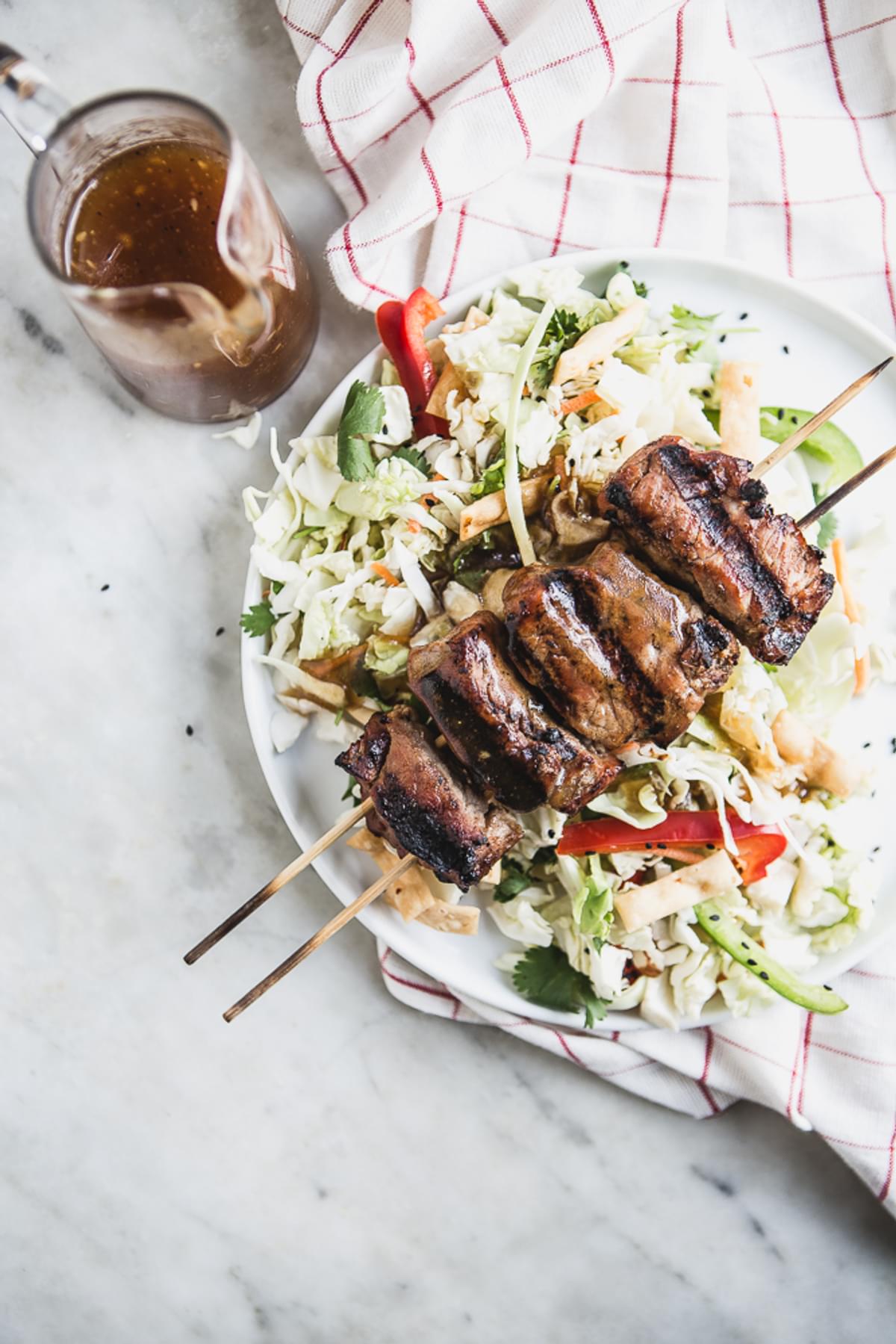 Asian Chopped Salad with Hoisin Marinated Pork Kabab on a plate with red and green bell peppers and sesame seeds
