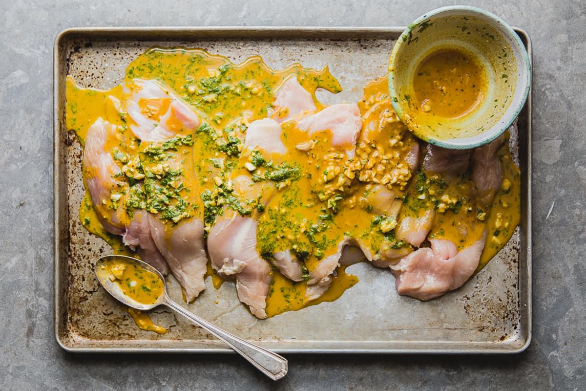 Raw chicken tenders marinating in a turmeric coconut sauce on a sheet pan