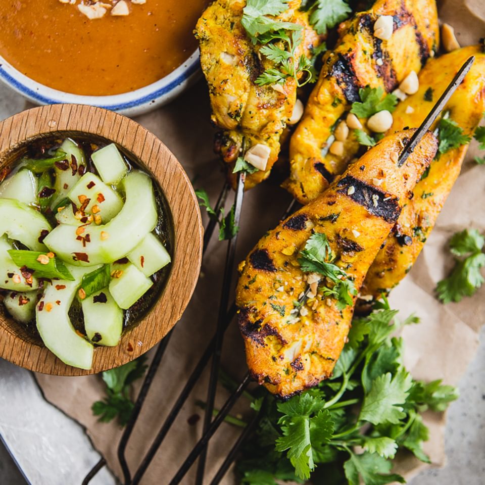 6 Chicken Satay on a plate served with Peanut Sauce and a Cucumber Salad