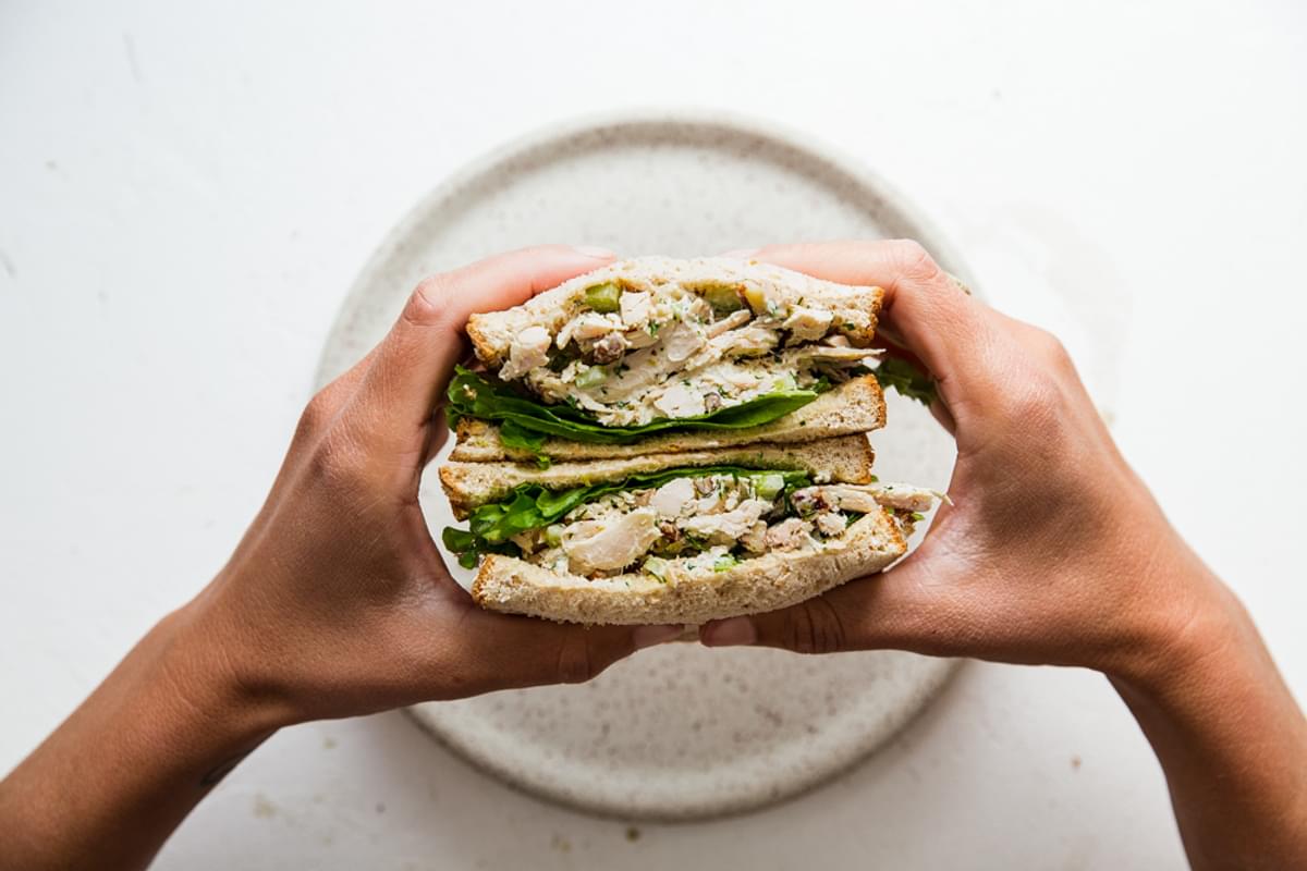 two hands holding classic chicken salad sandwich over a plate