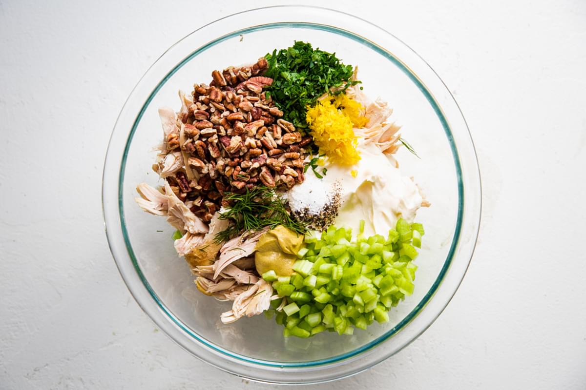 ingredients for chicken salad shredded chicken, mustard, lemon juice, tarragon, celery, pecans in a bowl