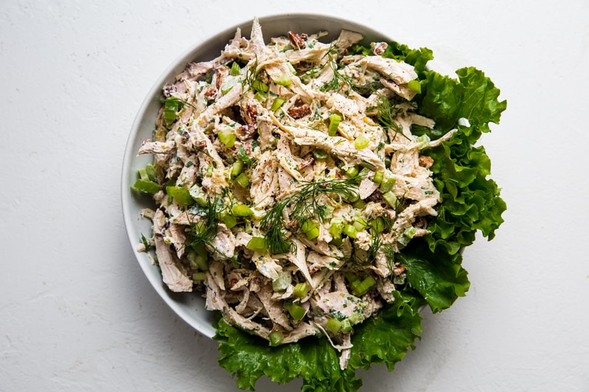 Chicken salad in a bowl shredded chicken, lettuce, lemon juice, tarragon, celery, pecans mixed together with lettuce