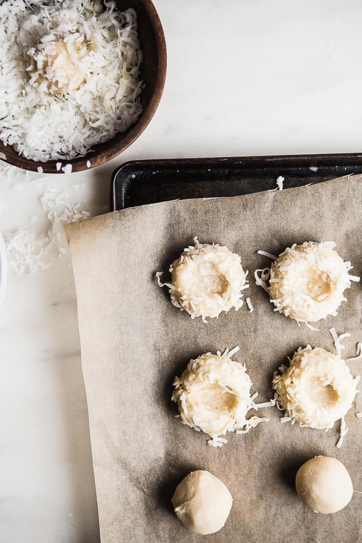 Coconut Thumbprint Cookies dough on a baking sheet with shredded coconut