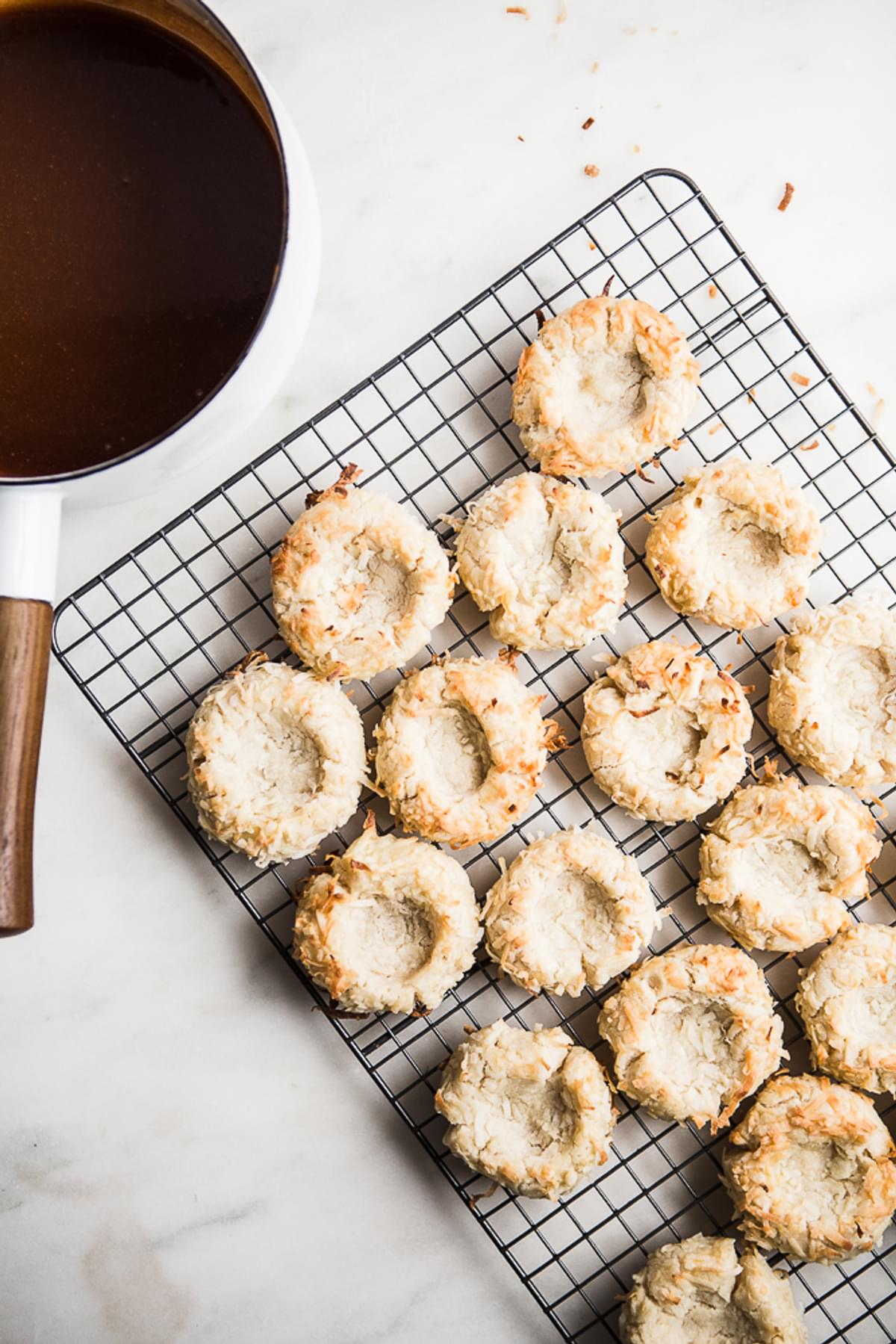 Coconut Thumbprint Cookies on a cooling rack with a pot of salted caramel next to it.