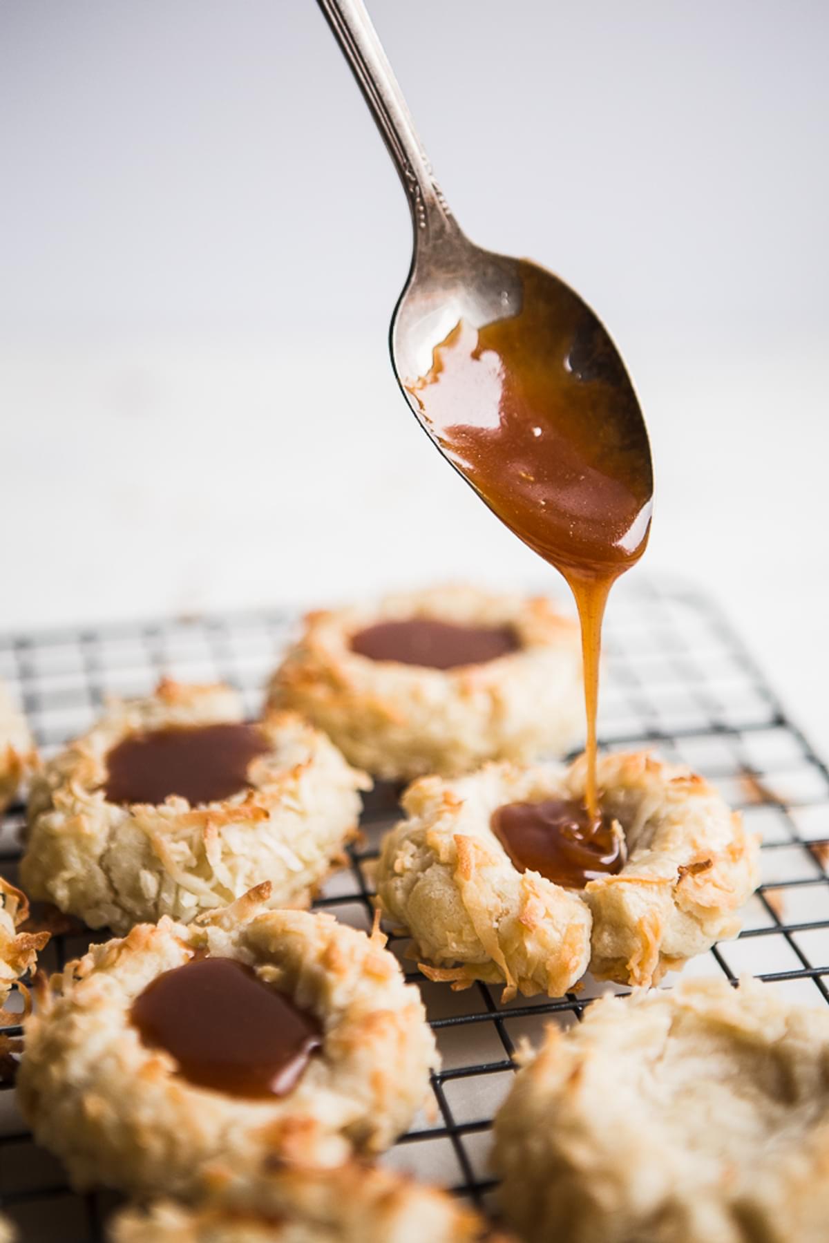 caramel being poured onto Coconut Thumbprint Cookies with Salted Caramel sauce