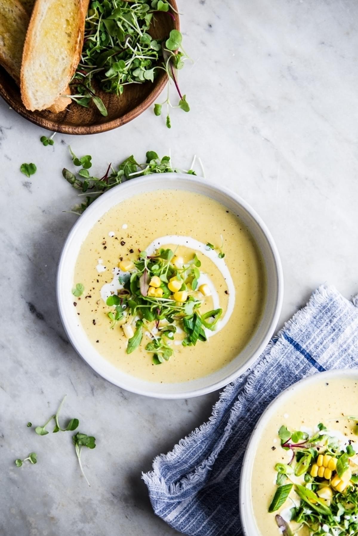 Corn and Leek Bisque soup with bread and micro greens in 2 bowls with a linen