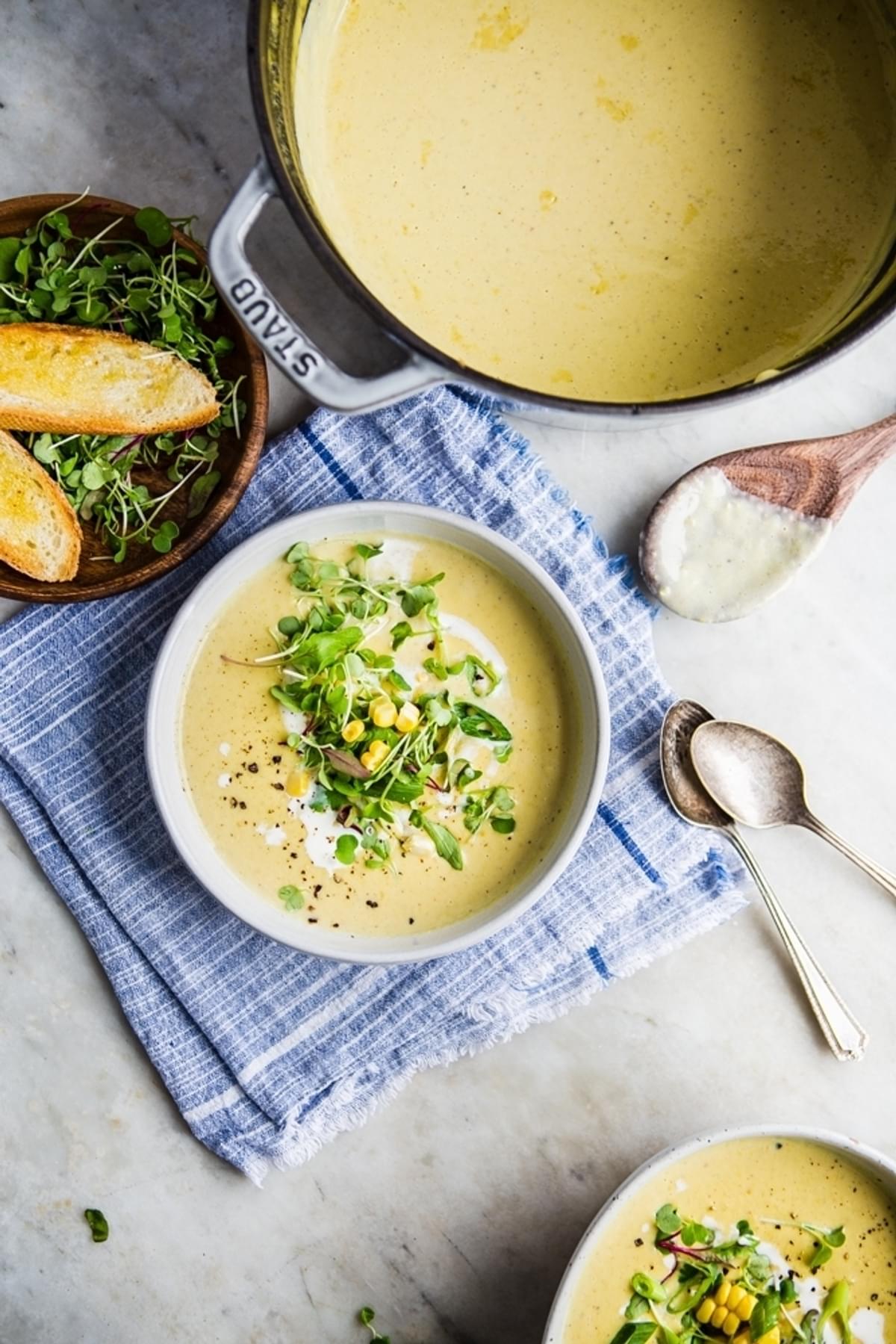 a soup pot full of Corn and Leek Bisque with 2 bowls and bread