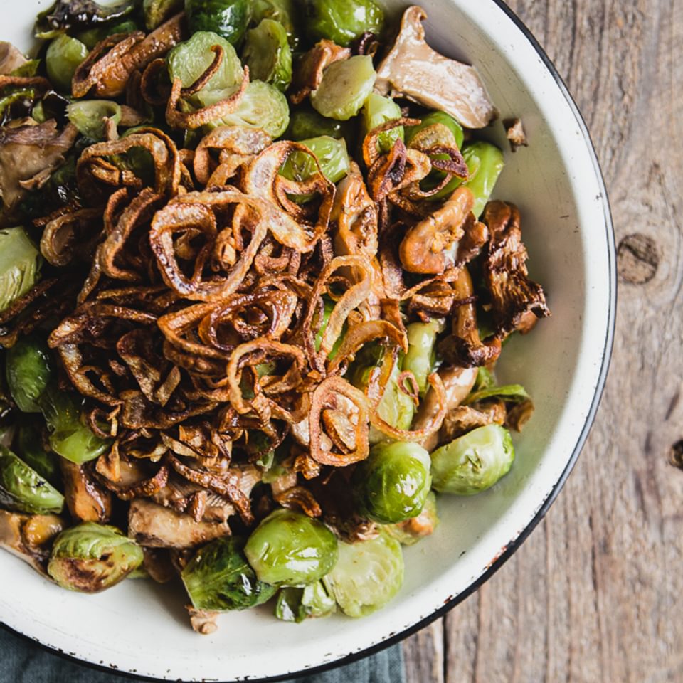 Creamy Brussels Sprouts with Wild Mushrooms and fried shallots in a bowl with a serving spoon
