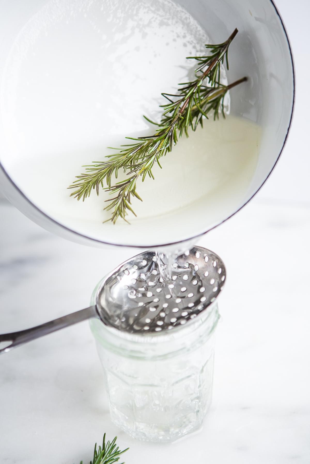 rosemary simple syrup being strained into a glass jar