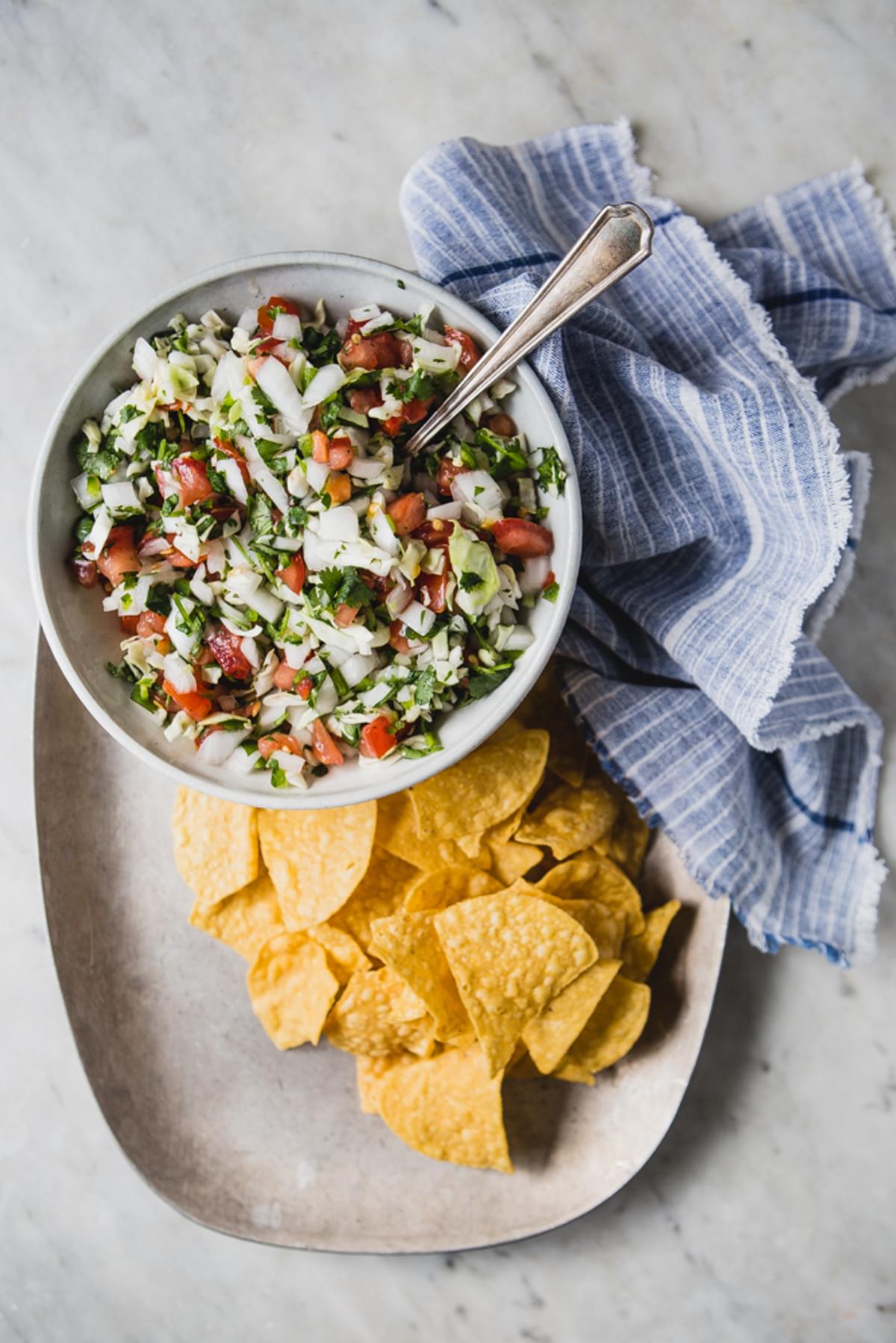 Bowl of Pico De Gallo with Cabbage on a plate with corn tortilla chips and blue linen