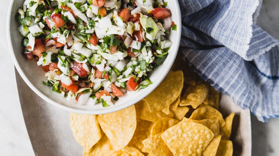 Pico De Gallo with Cabbage on a bowl with tortilla chips on a plater with a linen