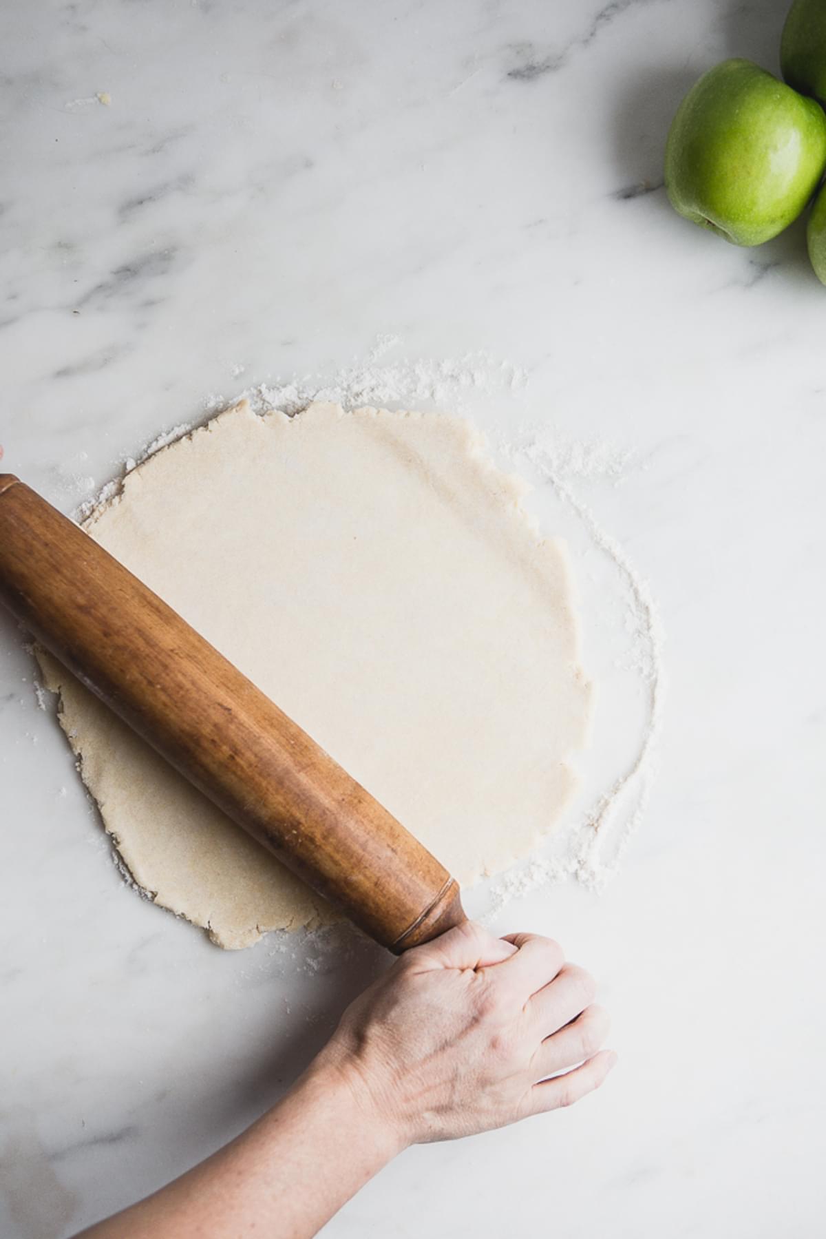 hands rolling out pie crust for apple pie
