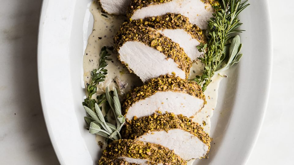 Pistachio Crusted Pork Tenderloin with White Wine Dijon Sauce on a plater with herbs and extra sauce in a dish